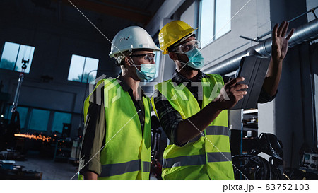 Industrial inspectors with face masks doing general check up at metal workshop, coronavirus concept 83752103