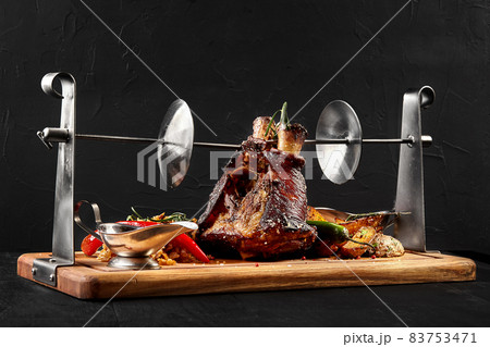 Roasted pork knuckle eisbein with braised boiled cabbage, potatoes, chili peppers and mustard on wooden cutting board, on a black background 83753471