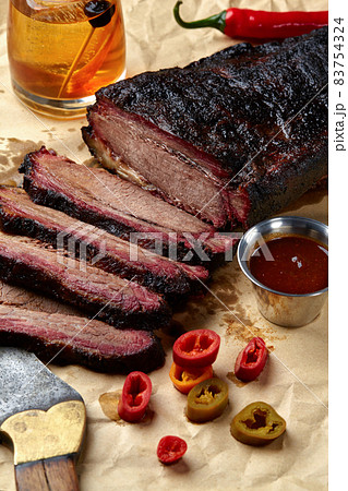 Fresh Brisket BBQ beef sliced for serving against a kraft paper background with sauce, hot peppers and corn. 83754324