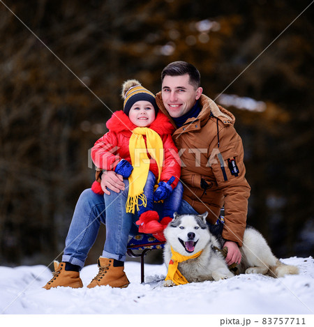 A father with a beautiful daughter and a husky dog are walking in the winter forest. 83757711