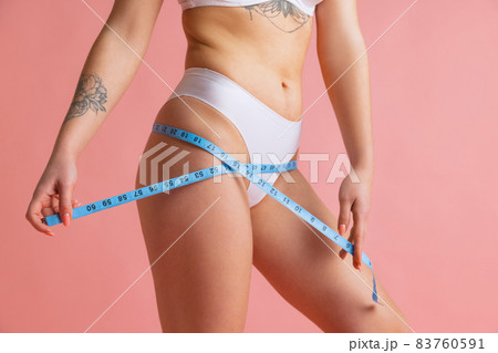 Close-up slim female body with well kept skin in white cotton panties using centimeter isolated over pink studio background. Close-up slim female body with well kept skin in white cotton panties using centimeter isolated over pink studio background. 83760591