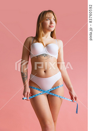 Portrait of beautiful young woman in white underwear using centimeter isolated over pink studio background. Portrait of beautiful young woman in white underwear using centimeter isolated over pink studio background. 83760592