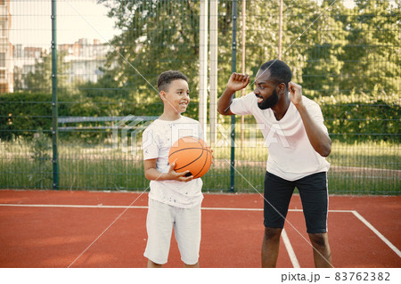 Black father with son playing basketball in basketball court together 83762382