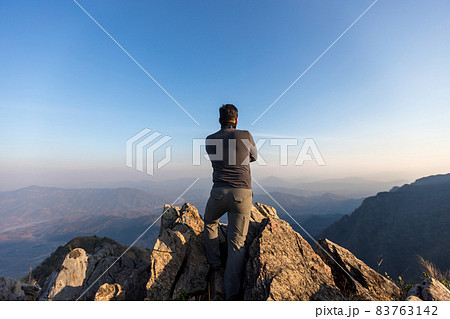 Young Man Standing on the edge of a cliff and enjoys the sunrise.  83763142
