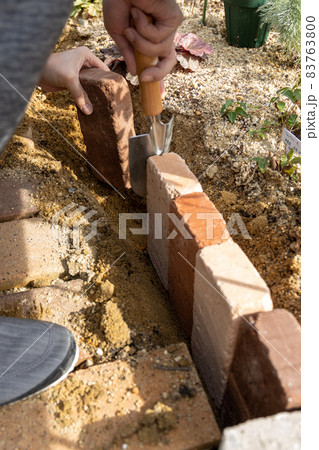 庭にレンガで花壇を作っている男性の手 83763800