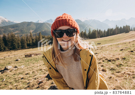 Young blond woman with sunglasses dancing in mountains. Freedom, happiness, travel and vacations concept, outdoor activities. Happy Girl wearing red hat and a yellow jacket 83764881