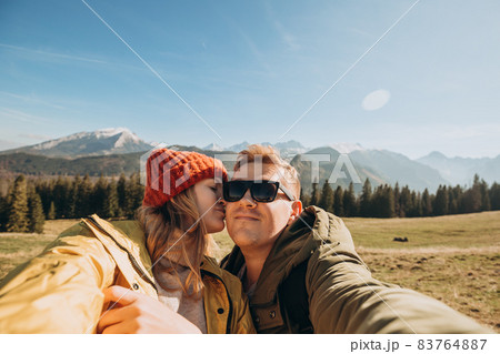 Couple making selfie photo high in the snow mountains enjoying the view. Freedom, happiness, travel and vacations concept, outdoor activities, she wearing in red hat and he a green jacket 83764887