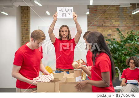 Young volunteers in red tshirts distributing donations in a sorting center Young volunteers in red tshirts distributing donations in a sorting center 83765646