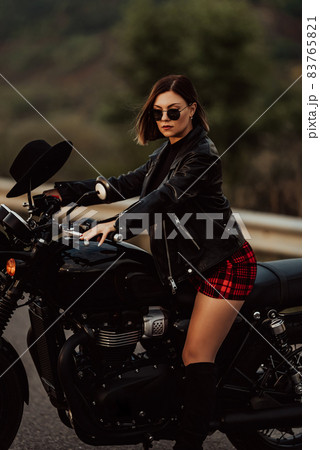 Portrait of stylish woman sitting on classic black retro-styled motorcycle while standing on road Portrait of stylish woman sitting on classic black retro-styled motorcycle while standing on road 83765821