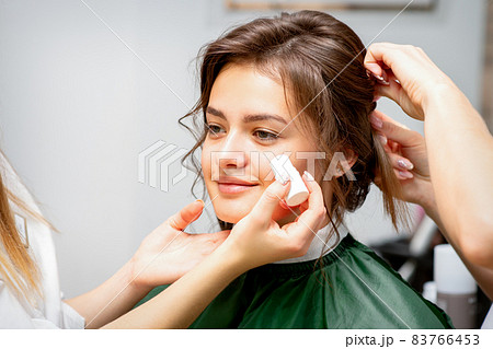 Makeup artist applying cream blush foundation tube on the cheek of the young caucasian woman in a beauty salon. 83766453
