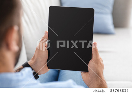 Middle-aged man sits on couch, resting and looking at tablet with blank screen, watch video or ad 83768835