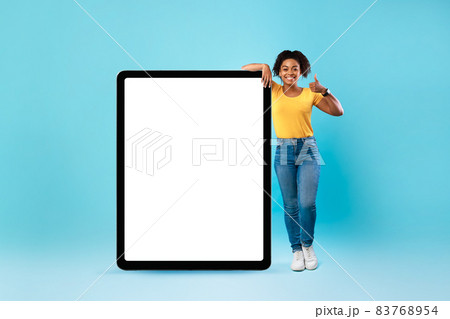 Happy black lady standing near huge tablet pc with empty screen, showing thumb up, recommending app or website, mockup Happy black lady standing near huge tablet pc with empty screen, showing thumb up, recommending app or website, mockup 83768954