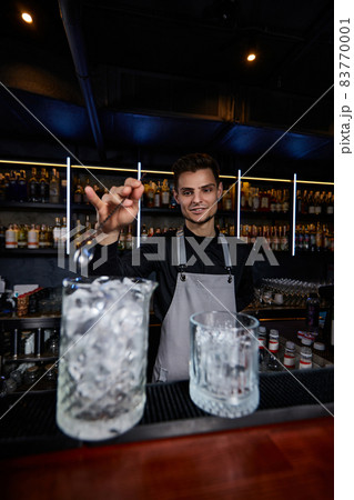 Barman stirring ice cubes in cocktail glass with spoon 83770001