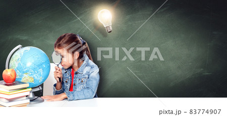 Curious little girl looking through magnifying glass on globe 83774907
