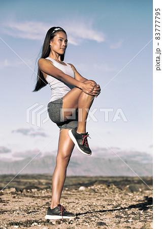Leg stretching exercise fitness runner woman doing running warm-up, hamstring muscles stretch standing wtih single knee to chest stretch. Female athlete preparing legs for cardio workout. 83777795
