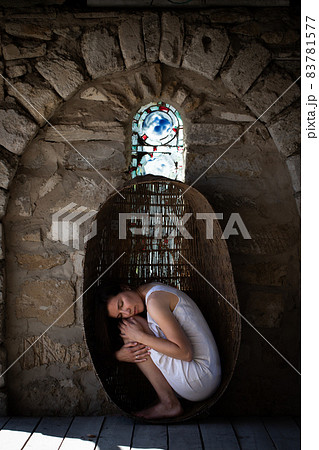 A woman sits in a large wicker basket, hugging her knees. The concept of motherhood, self-knowledge, awareness. A woman sits in a large wicker basket, hugging her knees. The concept of motherhood, self-knowledge, awareness. 83781577