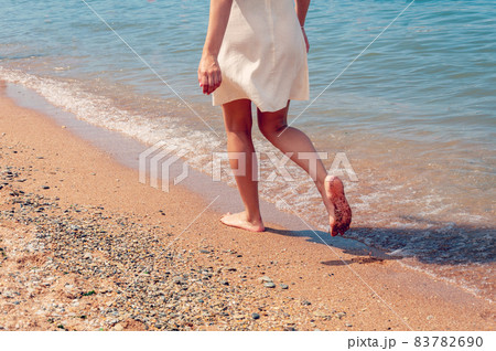 Woman walking on sand beach closeup. Beach travel. Woman walking on beach leaving footprints in the sand Woman walking on sand beach closeup. Beach travel. Woman walking on beach leaving footprints in the sand 83782690