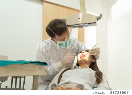 A dentist checking up Asian woman patient's teeth by using dental mouth mirror at hospital clinic. Teeth check up with dental tools. Doctor. Dentistry, medical and health. People. 83783667