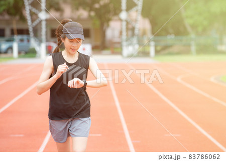 Portrait of young athlete runner woman running in the running track and she looking to her smart watch. Running track is a rubberized artificial running surface for track and field athletics. 83786062