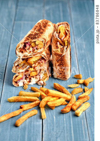 Shawarma chicken roll in a pita with fresh vegetables, cream sauce and french fries on wooden background. Selective focus Shawarma chicken roll in a pita with fresh vegetables, cream sauce and french fries on wooden background. Selective focus 83786848