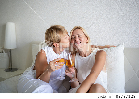 young woman with her mom sitting on the bed and drinking wine 83787128