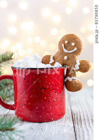 A red cup of winter hot drink with marshmallows and gingerbread man on a white wooden background with bokeh. A red cup of winter hot drink with marshmallows and gingerbread man on a white wooden background with bokeh. 83790850