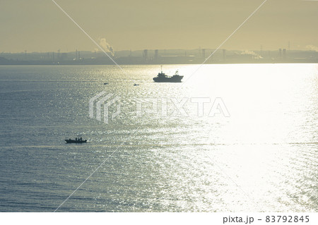早朝の朝日に照らされる東京湾、逆光の朝日に反射した海、工業地帯を抜ける船舶船 83792845