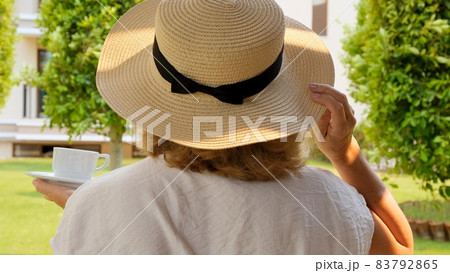 Senora female, age 50-55 in a straw hat holds a cup of hot drink and drinks coffee, sitting in the 83792865