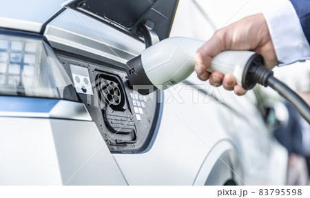 The driver of the electric car inserts the electrical connector to charge the batteries. 83795598