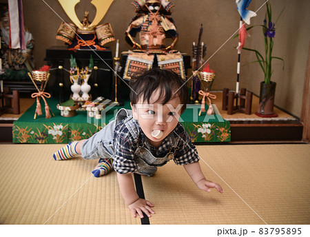 子どもの日、鎧兜の飾りのお猪口をくわえて逃げる赤ちゃん 83795895