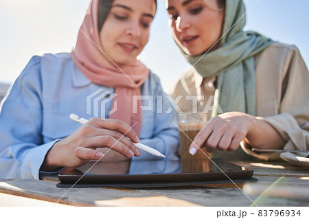 Concentrated girls in headscarfs holding stylus during the drawing at the tablet computer Concentrated girls in headscarfs holding stylus during the drawing at the tablet computer 83796934