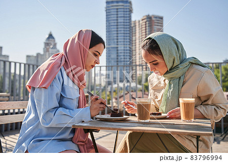 Two arabian girls in abayas sitting at the cafeteria and enjoying of their lunch Two arabian girls in abayas sitting at the cafeteria and enjoying of their lunch 83796994