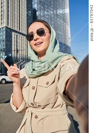 Woman gesturing and pointing with her hand at some buildings while having a video call 83797042
