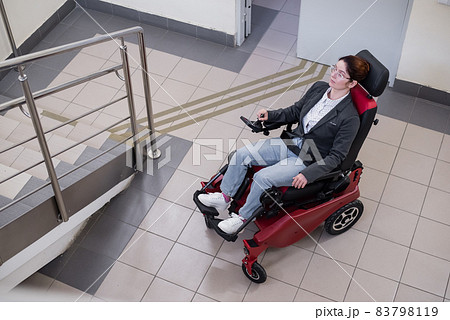 Caucasian woman in electric caterpillar wheelchair climbs up stairs. Caucasian woman in electric caterpillar wheelchair climbs up stairs. 83798119