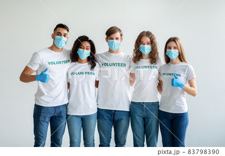 Group of happy multiracial people in masks and gloves showing thumbs up while posing over light studio wall Group of happy multiracial people in masks and gloves showing thumbs up while posing over light studio wall 83798390