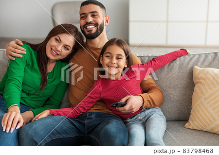 Cheerful young Arab family watching television sitting on sofa Cheerful young Arab family watching television sitting on sofa 83798468