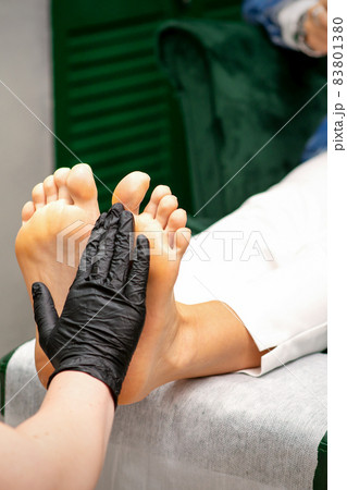 Moisturizing the feet. Hands of pedicure master in black gloves care about female feet. Foot massage. Pedicure beauty salon concept. Moisturizing the feet. Hands of pedicure master in black gloves care about female feet. Foot massage. Pedicure beauty salon concept. 83801380