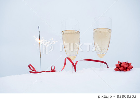 Two glasses with champagne and sparkler in snow Two glasses with champagne and sparkler in snow 83808202