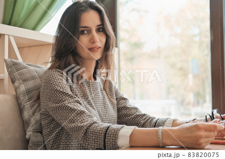 beautiful asian woman sitting in a cafe and waiting for lunch. young brunette woman looking at camera and smiling. copy space. 83820075