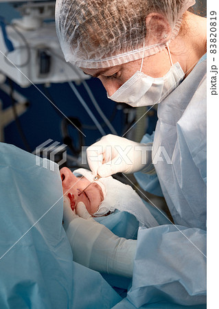 Close up of the face of a patient who is undergoing blepharoplasty. The surgeon cuts the eyelid and performs manipulations using medical instruments Close up of the face of a patient who is undergoing blepharoplasty. The surgeon cuts the eyelid and performs manipulations using medical instruments 83820819