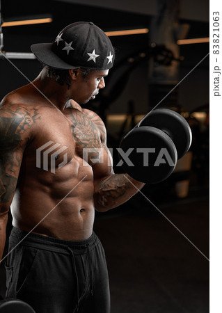 Strong and muscular dark skin man trains on modern equipment in gym. Portrait of muscular pumped up fitness trainer Strong and muscular dark skin man trains on modern equipment in gym. Portrait of muscular pumped up fitness trainer 83821063