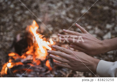 A woman warms her hands over a fire in a campsite. Journey to the forest A woman warms her hands over a fire in a campsite. Journey to the forest 83823250