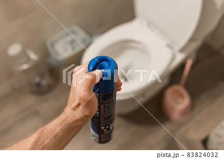 The guy's hand holds and sprays the air freshener in the toilet or bathroom. Home Hygiene Concept 83824032