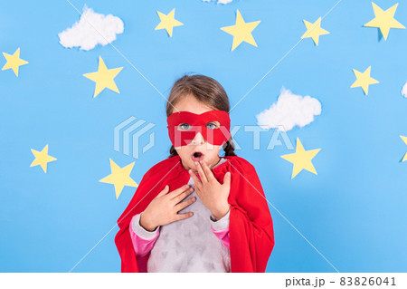 Little child plays superhero. Kid on the background of bright blue wall with white clouds and stars . Girl power concept. Little child plays superhero. Kid on the background of bright blue wall with white clouds and stars . Girl power concept. 83826041