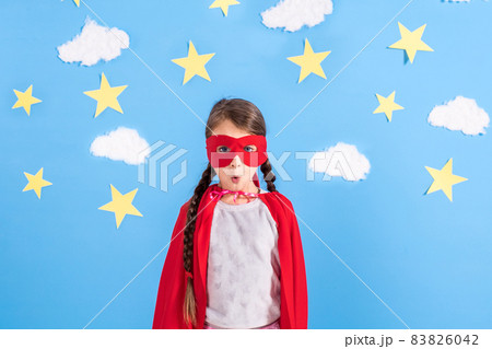 Little child plays superhero. Kid on the background of bright blue wall with white clouds and stars . Girl power concept. Little child plays superhero. Kid on the background of bright blue wall with white clouds and stars . Girl power concept. 83826042