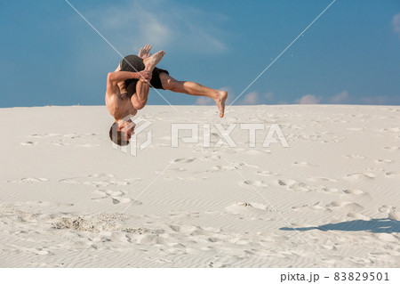 Portrait of young parkour man doing flip or somersault on the sand. 83829501