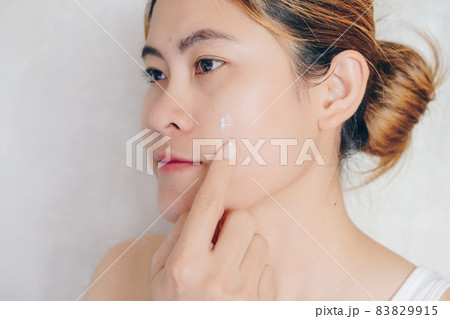 Close-up of young Asian woman applying moisturizer cream on her face. Conceptual of beauty and skin care. 83829915