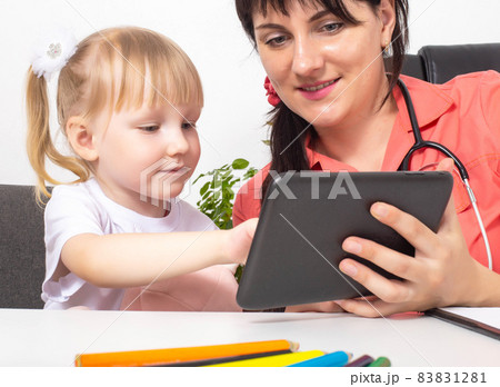 A woman doctor, a pediatrician, shows a 3-4 year old girl cartoons on a tablet. An individual approach to the treatment of each child. Pediatric medicine A woman doctor, a pediatrician, shows a 3-4 year old girl cartoons on a tablet. An individual approach to the treatment of each child. Pediatric medicine 83831281