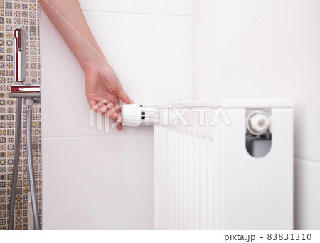 the woman turns on the heating radiator in the bathroom with a thermostat. Setting a comfortable temperature in the bathroom, copy space for text 83831310