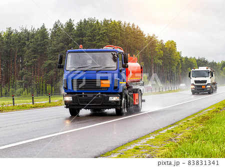 Two tanker trucks for transporting petroleum products drive on the highway with their headlights on in cloudy weather and rain in summer. Gasoline transportation concept, dangerous cargo Two tanker trucks for transporting petroleum products drive on the highway with their headlights on in cloudy weather and rain in summer. Gasoline transportation concept, dangerous cargo 83831341